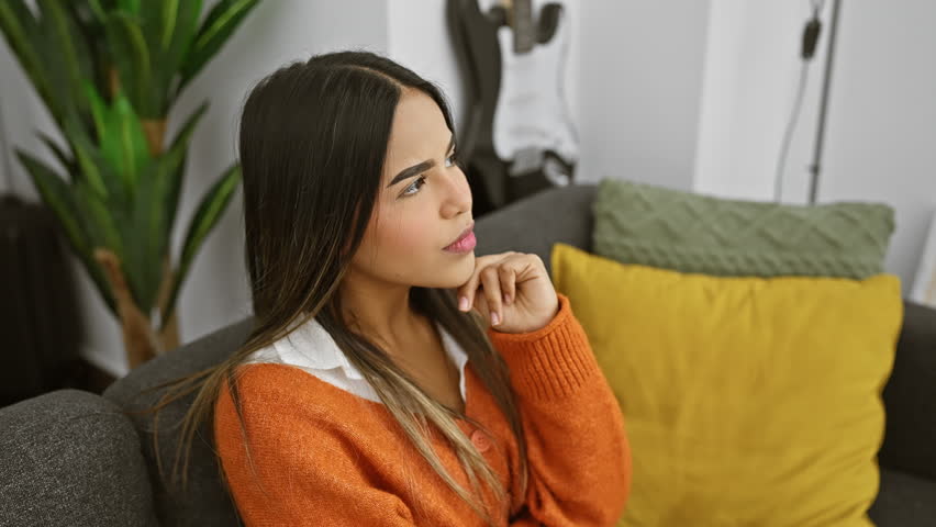 Young beautiful latin woman wearing sweater sitting on sofa thinking concentrated about doubt with finger on chin and looking up wondering at home Royalty-Free Stock Footage #3432100331