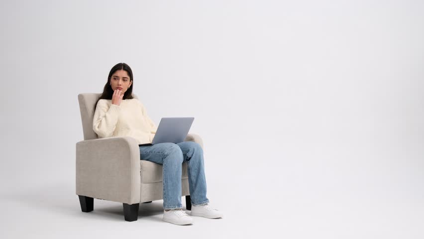 Puzzled Caucasian woman using laptop in armchair isolated on white background