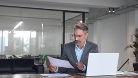 Focused Hispanic businessman with paperwork in office. Concentrated European male business man accountant analyst holding documents, work at laptop computer doing online trade market tech research.  - Powered by Shutterstock - Get 15% off with code: PIKWIZARD15