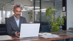 Serious mature European business man ceo trader using computer, typing, working in modern office, doing online data market analysis, thinking planning tech strategy looking at laptop with copy space.
