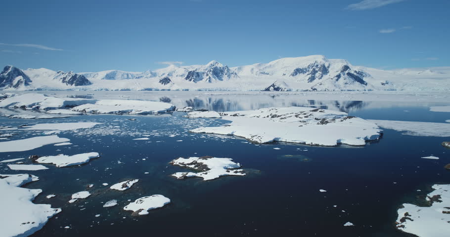 Antarctica landscape in sunny day aerial view. Fly over the untouched wilderness of Antarctic Peninsula. Blue sky, snow covered mountains, cold ocean. Breathtaking harmony of untouched polar nature