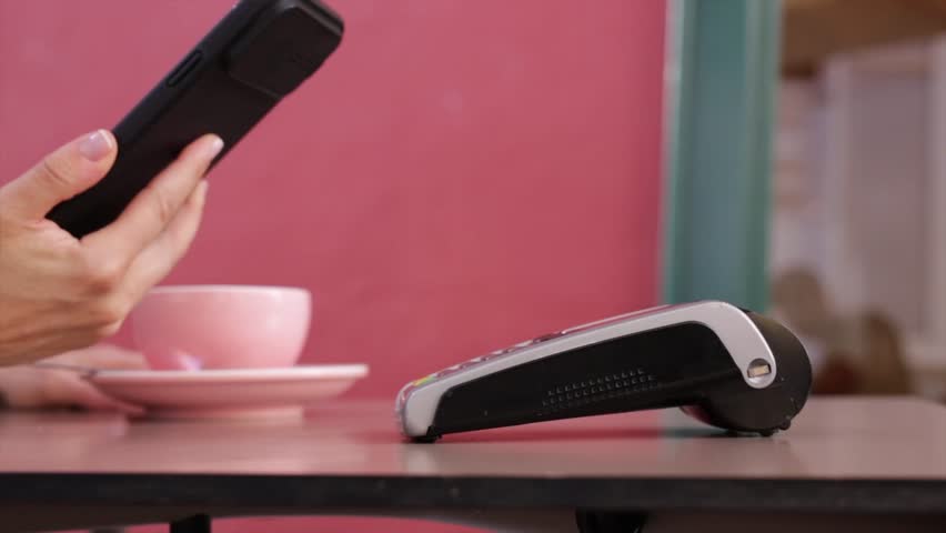Happy woman paying with NFC technology as her mobile phone at payment terminal