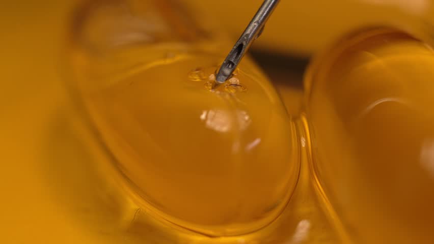 Close-up macro needle puncture pierces and injects a gelatin capsule with omega 3 fish oil pill