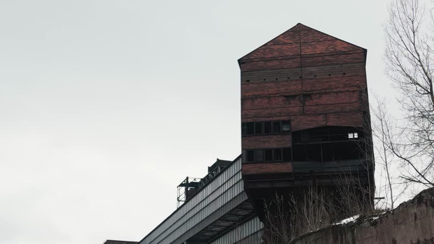 Large, bricked, and weathered industrial structure towering against a cloudy sky