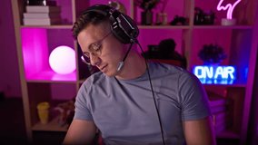 A young hispanic man wearing headphones in a neon-lit gaming room at home, looking focused and professional as a gamer.