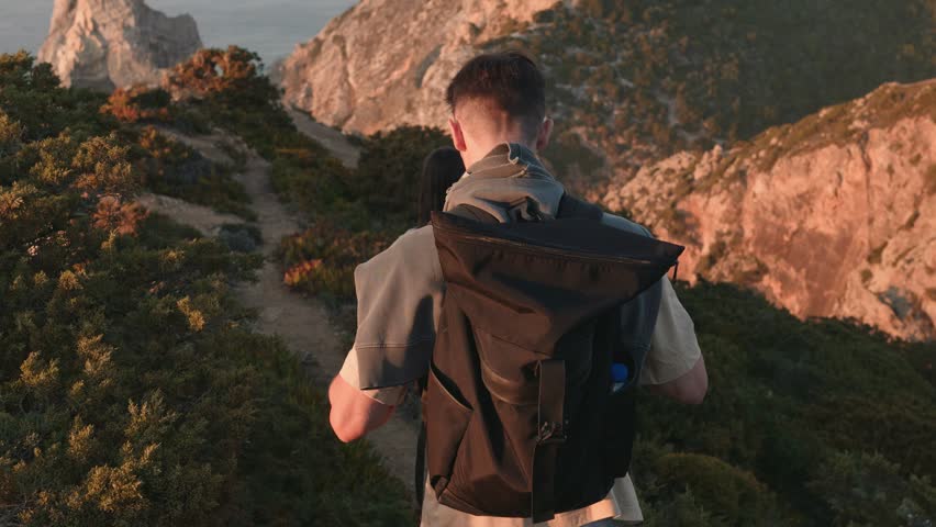 A couple hiking on a mountain trail at sunset, surrounded by lush greenery and overlooking the ocean, capturing a sense of adventure and companionship.