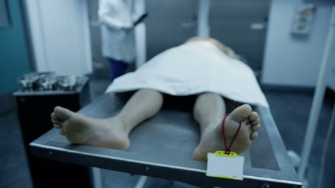 The lifeless naked body of a young mixed race male is laid out on the autopsy table, ready for the medical examiner to begin his work. In slow motion.
