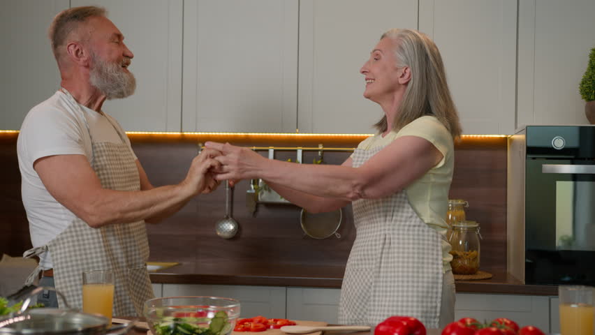 Caucasian love couple happy retired family old mature man and woman cooking in home kitchen romantic dancing grandmother grandfather celebrating anniversary romance dance to music have fun laughing Royalty-Free Stock Footage #3432412135
