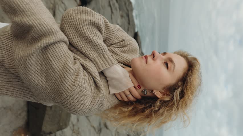 A peaceful woman in a knitted sweater with eyes closed, savoring a quiet moment and dancing against a soft, natural backdrop. Represents tranquility and comfort. Royalty-Free Stock Footage #3432424583