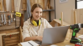 Smiling woman with headphones using a laptop in a wood workshop surrounded by tools - Powered by Shutterstock - Get 15% off with code: PIKWIZARD15