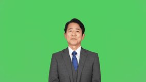 Asian middle-aged man in a business suit giving a speech in front of a green background for chroma key composition.