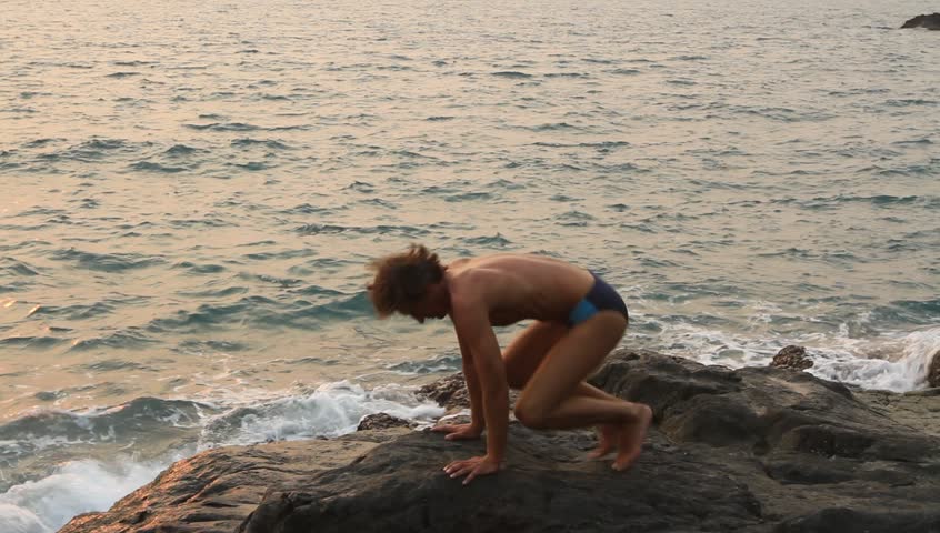 Man doing yoga exercise on the rocks by the sea (HD)