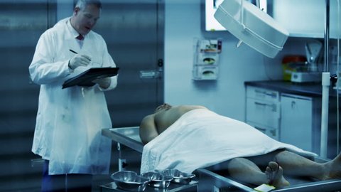 The lifeless naked corpse of a young mixed race male is laid out on the autopsy table, being inspected the medical examiner.