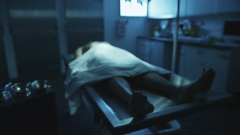The lifeless naked corpse of a young mixed race male is laid out on the autopsy table, all alone in the dark and with a tag on the toe.