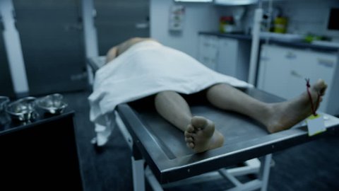 The lifeless naked corpse of a young mixed race male is laid out on an autopsy table, all alone and with a tag on the toe.