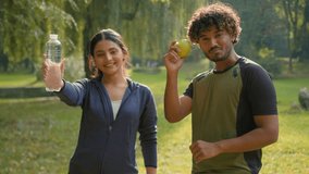 Indian man and woman relaxing after sports together in park outdoors Arabian fitness couple friends in city sport happy people showing holding apple fresh healthy fruit and bottle of water lifestyle - Powered by Shutterstock - Get 15% off with code: PIKWIZARD15