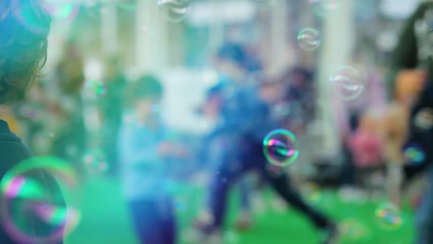 Children play and run among soap bubbles generated with a professional bubble machine. Royalty-Free Stock Footage #3432919373