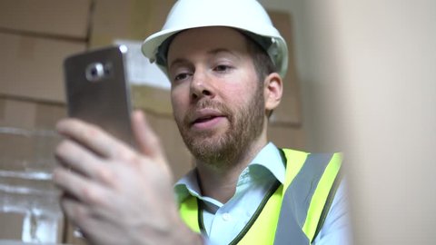 A Distribution Manager Has Mobile Phone Video Call Regarding Delivery In Warehouse. Professional Male Using Smartphone Technology At The Workplace.
