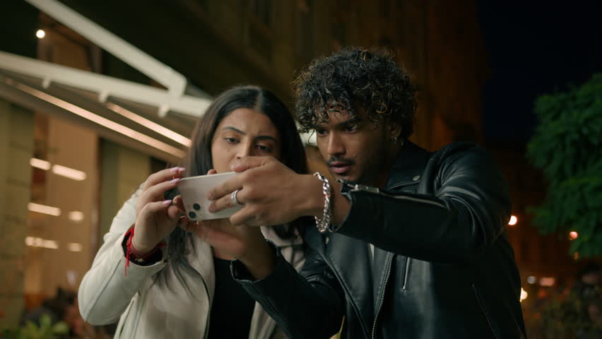 Confused puzzled man woman tourist travelers in night evening city Indian Arabian couple lost in street town travel tour trip guy girl using mobile phone navigator app online map GPS navigation point