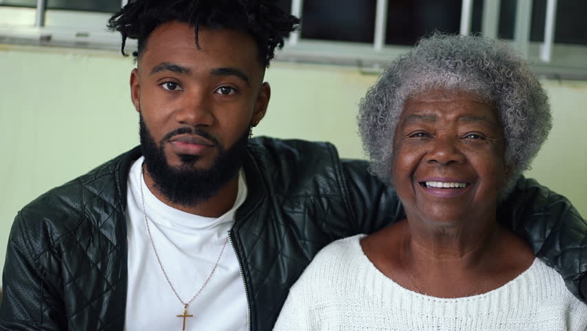 African American young grandson embracing his elderly gray hair grandmother portrait faces looking at camera in genuine loving moment, tender arm around shoulder, intergenerational bond Royalty-Free Stock Footage #3433053383