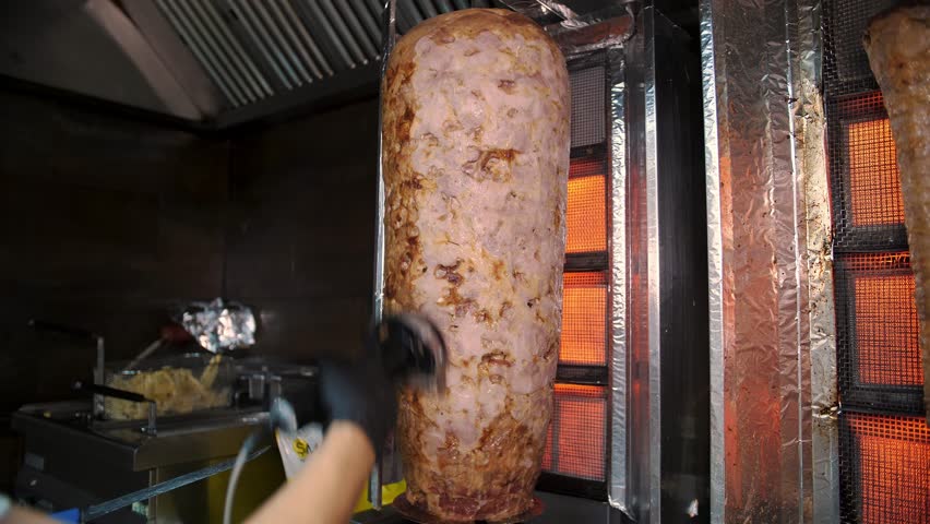 A cook cuts meat to make shawarma, gyros, doner kebab. Cooking meat on a skewer