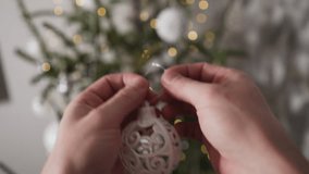 POV of hands hanging a delicate, filigree Christmas ball on a tree with glowing lights - Powered by Shutterstock - Get 15% off with code: PIKWIZARD15