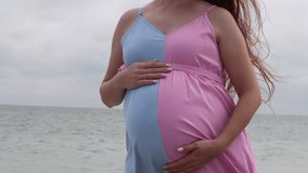 Video 4K close up of pregnant belly. Boy or girl? pink and blue dress. Pregnant woman holding her belly near the ocean. 