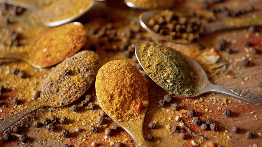Falling Dry Spices on Spoons with Colorful Spices Rotating on Wooden Background. Abundance of dried Indian herbs. Allspice, black peppercorns, dill, paprika, turmeric, oregano. Ingredients. Texture.