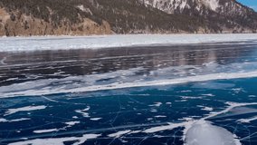 Aerial drone view frozen winter Lake Baikal. Blue transparent ice deep cracks top view. Natural cold background of ice. Winter abstract background. High quality 4k footage