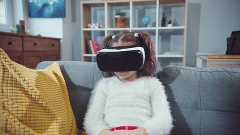 Little girl sitting on the sofa with glasses virtual reality in home smiling game kid modern play reality technology display emotion high tech immersion innovation slow motion
