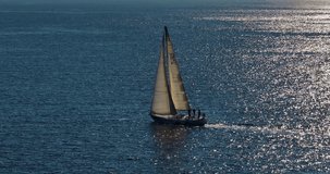 White modern sailing yacht in blue warm water. A view from a drone of a ship with a sail plowing the depths of the ocean. Traveling by sea in the rays of the setting sun. Luxurious lifestyle