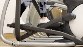 Cardio workout on an elliptical trainer. Horizontal video of walking female legs on orbitrek, side view. Middle-aged woman goes on an elliptical exercise machine.