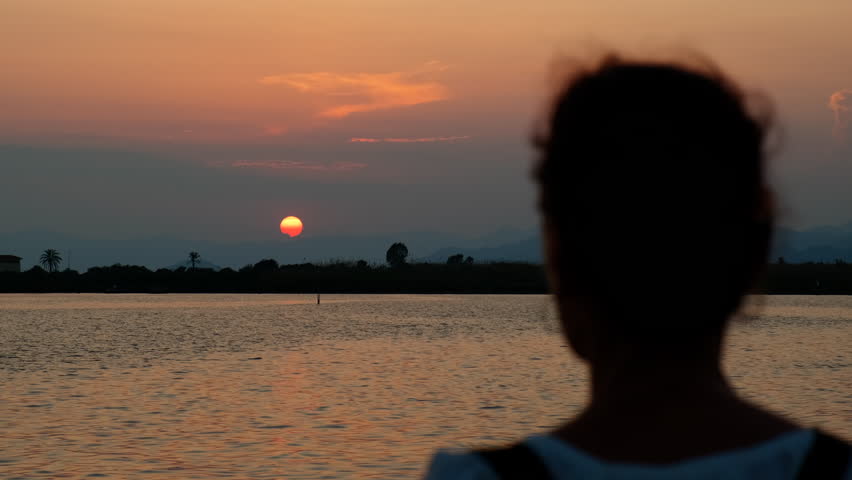 Woman silhouette against morning lake. A view of female silhouette enjoy the warm lake waves during sunset time.