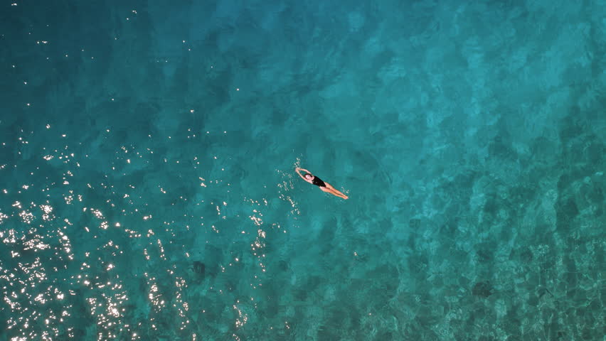 Serene view of woman swimming in sea water. A Relaxing Top-Down View of turquoise ocean expanse.