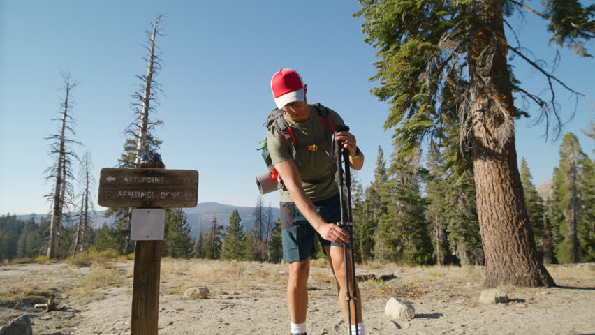Hiker adjusting his poles and preparing himself for the hike, with a trail sign in the woods. Sky Plant Tree Landscape on a sunny clear day with a blue sky, Yosemite, California, USA Royalty-Free Stock Footage #3433395703