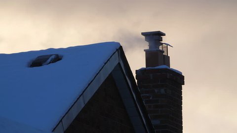 Winter chimney with smoke and snowy rooftop. East York, Toronto, Canada.
