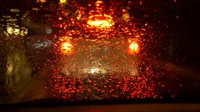 the rain streams on the front window of the windshield window of the car stop alongside the road with beautiful colorful blurry traffic lights off the road. 4k