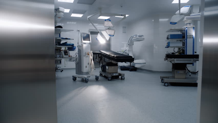 Dolly shot of operation block in modern clinic with advanced equipment ready for surgery. Operating table, LED lamps, life support machine. Bright operating room in hospital or medical facility. Royalty-Free Stock Footage #3433542395