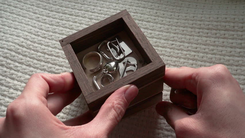 Female hands take silver necklace out of wooden casket box. Jewelry box fulls with earrings, pendants, chains. Close-up shot, daytime natural light. Sword pendant.