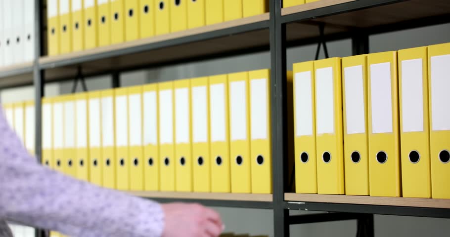 Woman secretary takes yellow folder with documents from shelf. Woman in office working with documents Royalty-Free Stock Footage #3433572455