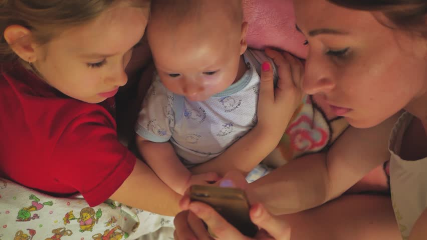 A young mother with her daughter and little son watching funny photo on cellphone together.