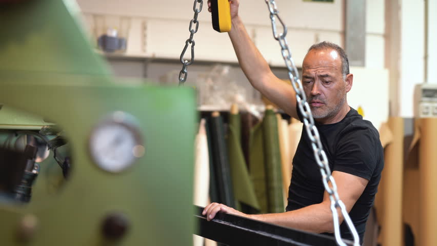 caucasian labor controlling a mechanical Overhead crane for moving heavy stuff inside a factory working class concept