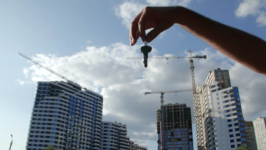 Real estate purchase concept. A male hand holding the key to a new apartment and throwing it to female hand with bracelets against the backdrop of a high-rise building under construction. Royalty-Free Stock Footage #3433654523