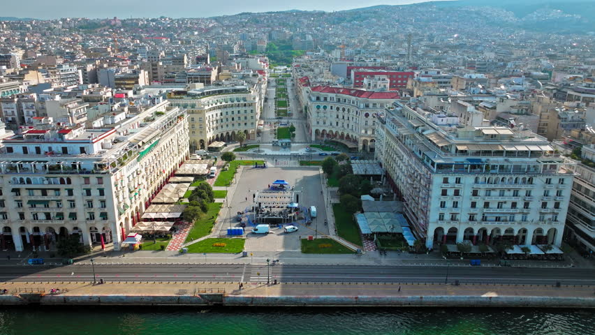 Aerial view of Vast, waterfront public square Aristotelous in Thessaloniki. View from above of ample, paved square surrounded by Neoclassical buildings, with a green park in the middle.