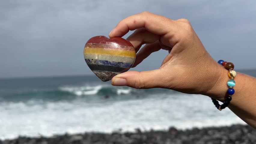 woman meditating on wild beach shore and holding crystal heart