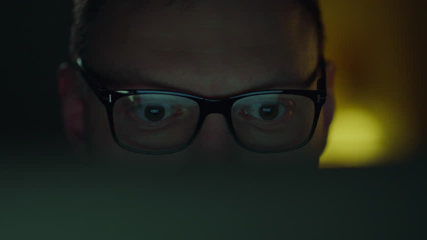 Under the light of a laptop computer screen, a programmer wearing glasses works hard at night. His face expresses deep concentration, the reflection of the data is visible in his glasses Royalty-Free Stock Footage #3433751853