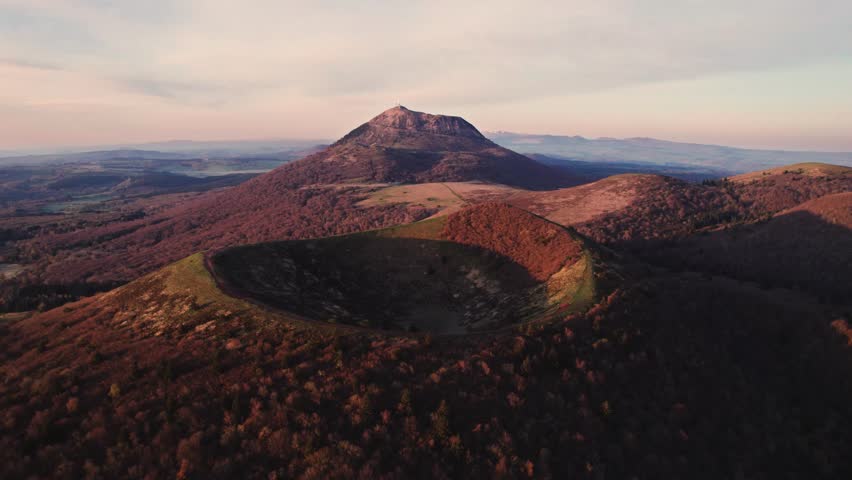 drone shot flying over puy pariou and revealing the Puy de Dome in the background at sunrise, Clermont Ferrand, Auvergne, France