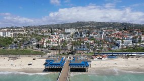 4k Aerial Video, left-to-right showing train passing San Clemente Pier and beach and shops in Orange County, towards San Diego, California,.