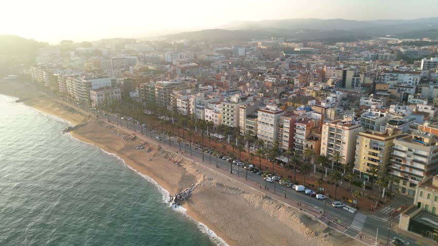 Beautiful gold sunset over famous city Lloret del Mar. Travel destination in Spain and one of the most famous beaches from Catalonia. Drone tracking left. Sun in the left corner. Panoramic view.