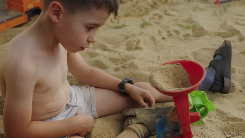 Cute little caucasian boy playing with constructor toy in the sand, outdoors. The child having fun on the playground.